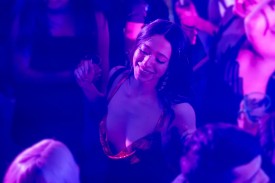 A woman bathed in blue, purple, and pink light dances in a club in a red sequined dress in a still from Sean Baker's Anora.